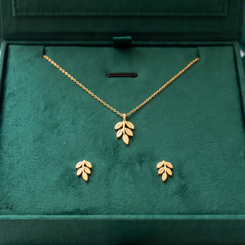 Close-up of a gold leaf necklace and earrings on an emerald velvet pad