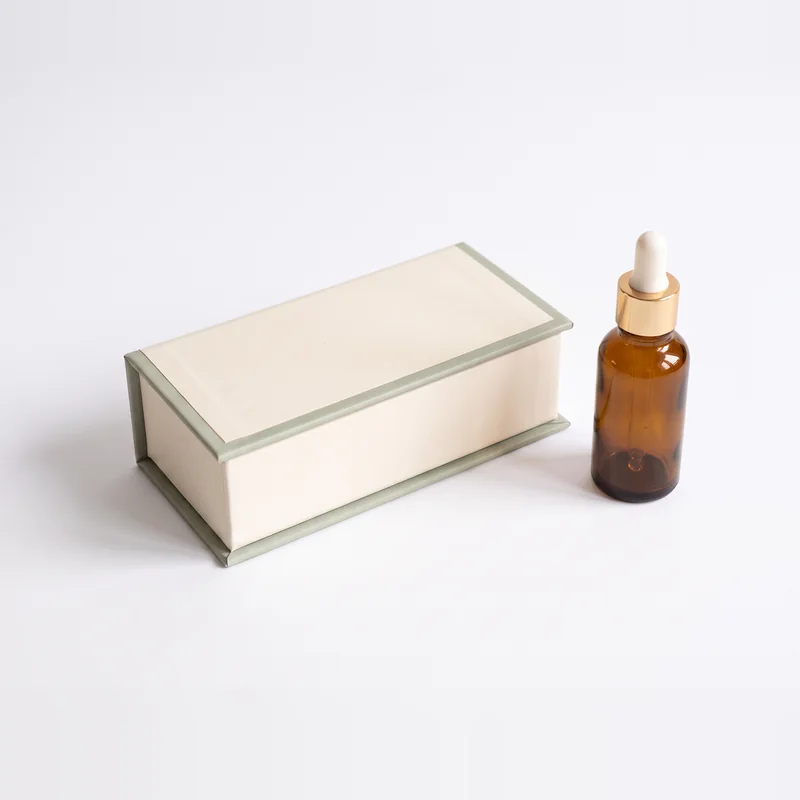 Closed ivory gift box with sage trim beside an amber dropper bottle